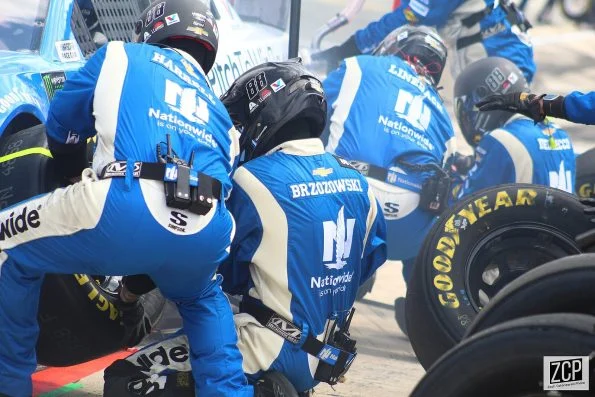 A pit crew in blue Nationwide uniforms changing tyres on Alex Bowman's number 88 Chevrolet during a pit stop.