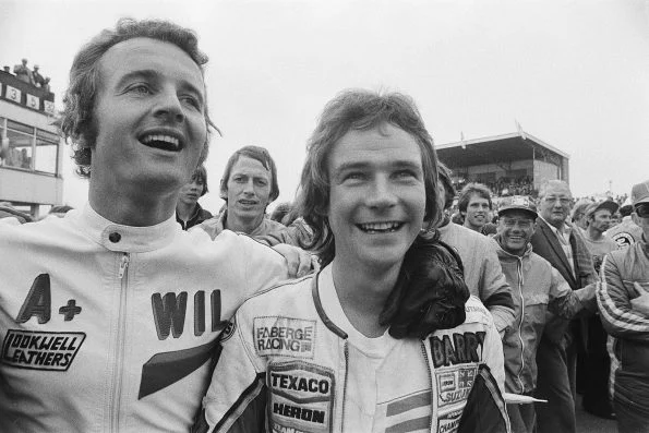 Barry Sheene in Texaco Heron team leathers standing beside Wil Hartog after the Dutch TT at Assen, spectators crowded behind them.