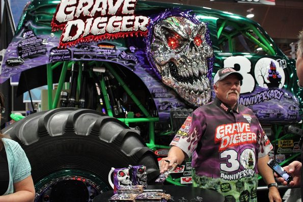 Dennis Anderson at a signing table in front of the 30th Anniversary Grave Digger truck and its chrome skull.