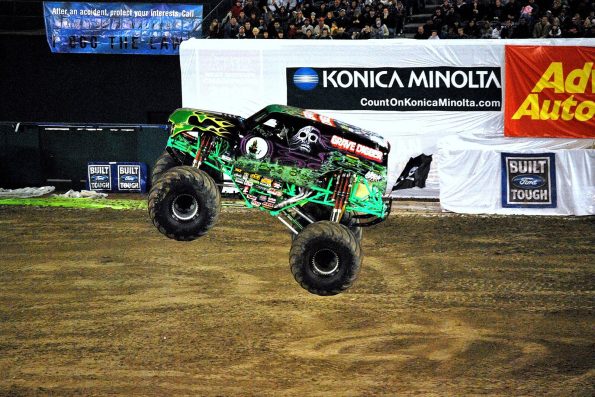 Dennis Anderson's green and black Grave Digger monster truck with its front wheels in the air on stadium dirt.
