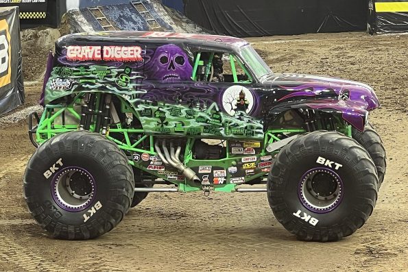 Dennis Anderson's purple and green Grave Digger XXXIX monster truck is shown in a detailed, full side-on view within an arena, featuring massive BKT tires.