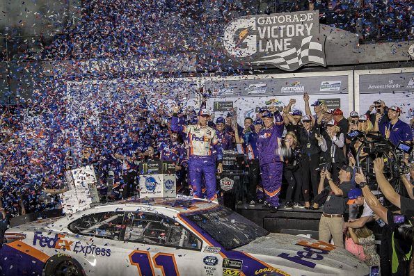 Denny Hamlin standing on his number 11 FedEx Express Toyota in Gatorade Victory Lane amid confetti, his team crowded around after winning the 2019 Daytona 500.