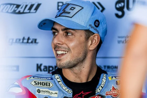 Fabio Di Giannantonio smiling, wearing a light blue cap bearing the number 49 and Gresini team kit.