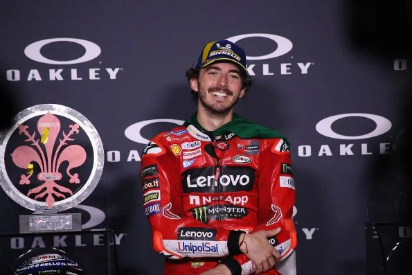 Francesco Bagnaia in red Ducati Lenovo leathers and a winner's cap, smiling beside the Mugello trophy after the race.