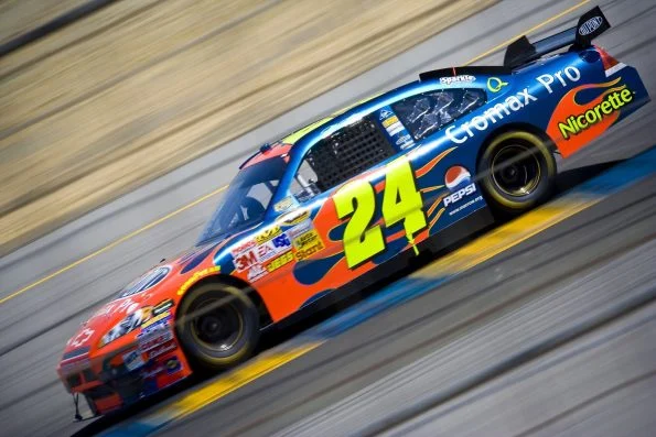 Jeff Gordon's number 24 DuPont Chevrolet in blue and orange flame livery, at speed with the background blurred.