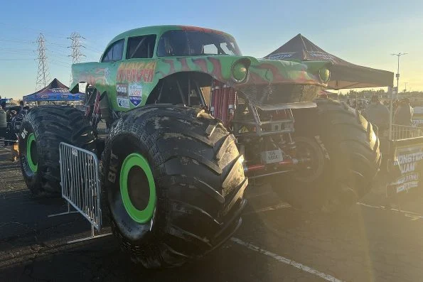 Jim Koehler's green Avenger monster truck with its 1957 Chevrolet Bel-Air body and flame graphics, parked in an outdoor paddock at dusk.