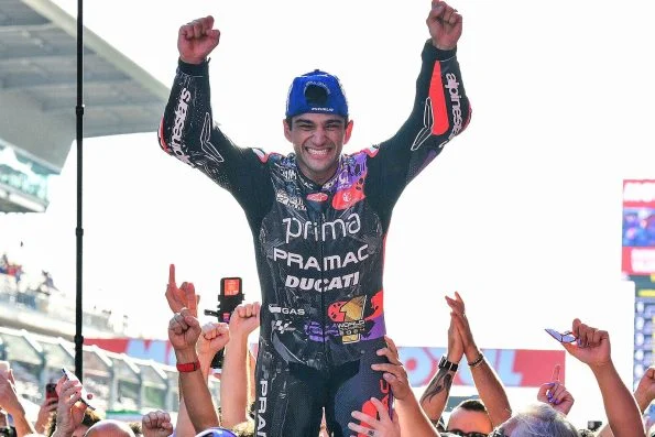Jorge Martín in Prima Pramac Ducati leathers with both arms raised in celebration, surrounded by fans and photographers.