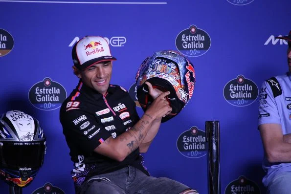 Jorge Martín in Aprilia Racing team clothing at a press conference, holding up a specially painted crash helmet.