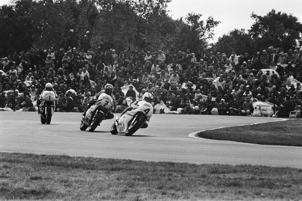 Kenny Roberts (carrying No. 1) corners in line with two other 500cc riders (No. 7 and No. 4) in front of a packed grandstand at Assen.
