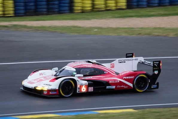Kévin Estre driving the number 6 Porsche Penske Motorsport Porsche 963 hypercar in white, pink and red livery, on track at Le Mans.