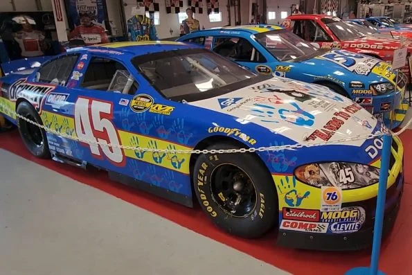 Kyle Petty's blue number 45 Victory Junction Dodge, its bodywork covered in children's handprints and drawings, on display.