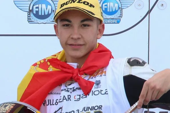 Raúl Fernández on the podium of the 2018 CEV Moto3 race at Valencia, wrapped in a Spanish flag and holding his helmet, wearing a Moto3 Junior World Champion 2018 vest.
