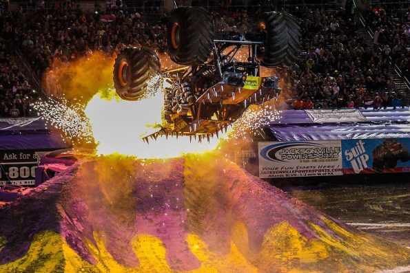 Tom Meents driving the Maximum Destruction monster truck upside down mid-backflip above a burst of pyrotechnics.