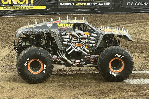 Tom Meents driving the Max-D monster truck with spiked silver bodywork and a skull face, side-on on arena dirt.