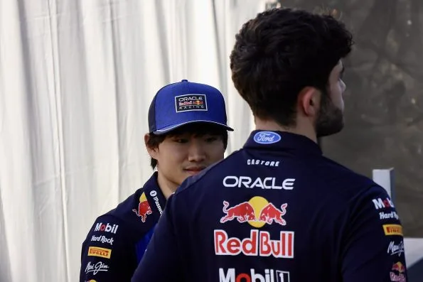 Yuki Tsunoda in an Oracle Red Bull cap and team shirt in the paddock, a team member beside him.