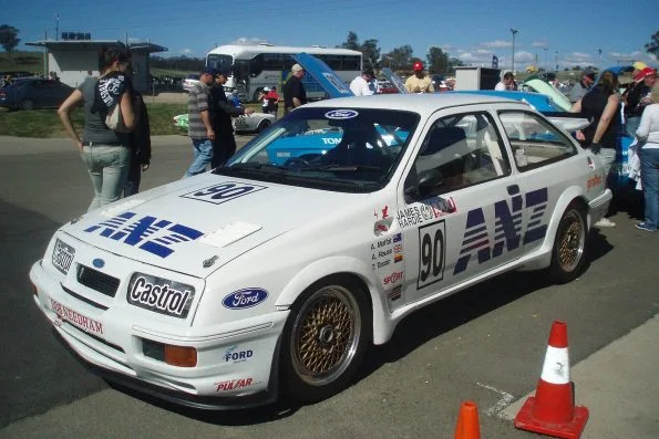 The white number 90 ANZ and Castrol Ford Sierra RS500 Cosworth, with A. Moffat, A. Rouse and T. Tassin listed on the door, parked at an outdoor display with spectators around it.