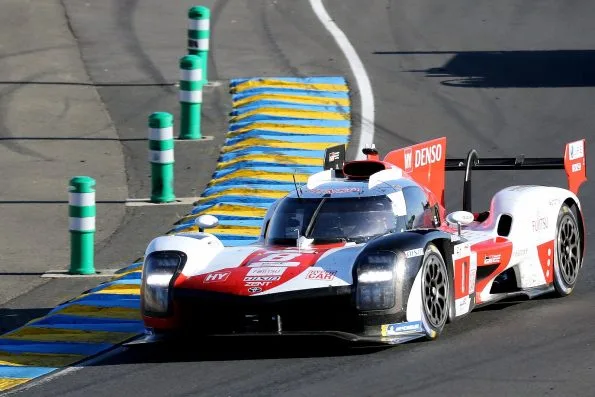 The white and red Toyota GR010 Hybrid, car 8, through the Esses at the 2022 24 Hours of Le Mans, alongside the blue and yellow kerbing, in the race Sébastien Buemi, Brendon Hartley and Ryō Hirakawa won.