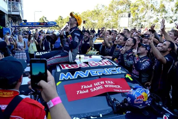 Jamie Whincup standing on his Red Bull Racing Australia Holden surrounded by team members photographing him, after winning the 2013 V8 Supercar Championship