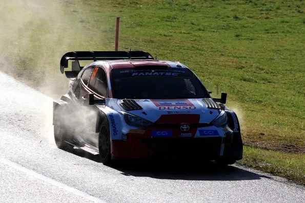 Kalle Rovanperä's Toyota GR Yaris Rally1, car 69, throwing up spray on a damp asphalt stage at the 2023 Central European Rally, backlit by low autumn sun.