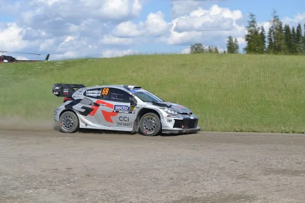 Kalle Rovanperä's silver Toyota GR Yaris Rally1, car 69, on the gravel of the Ouninpohja stage at Rally Finland in 2025, a helicopter parked on the crest behind.