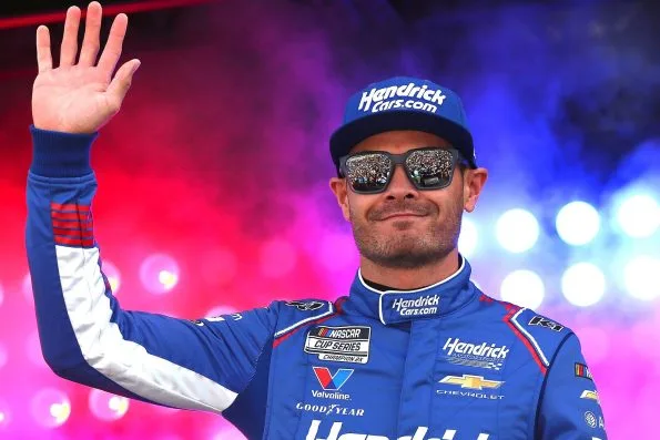 Kyle Larson waving in his HendrickCars.com race suit and cap during driver introductions at Las Vegas Motor Speedway in 2026.