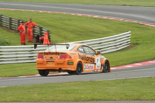 The orange number 1 Halfords Honda Integra of Matt Neal at Oulton Park during the 2006 British Touring Car Championship, marshals behind the barrier.