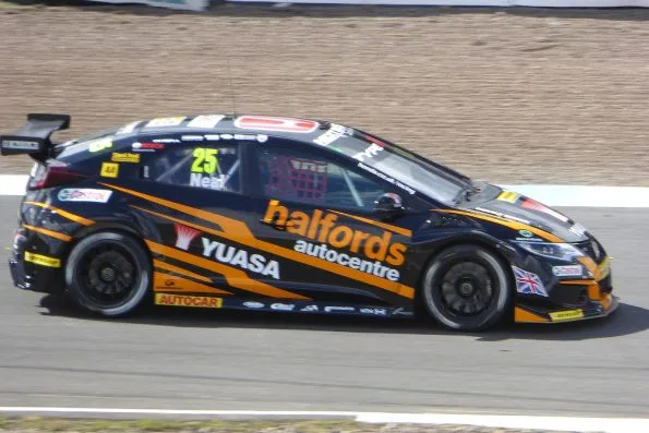 The black and orange number 25 Halfords Yuasa Honda Civic of Matt Neal at speed at Knockhill in 2017, his name above the door.