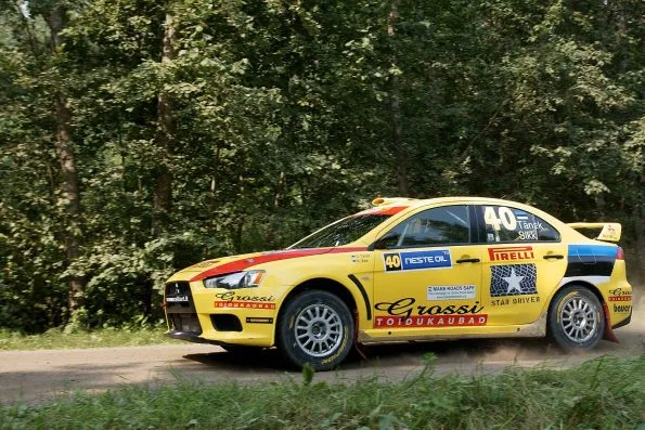 Ott Tänak's yellow Mitsubishi Lancer, car 40, on a forest gravel road at the Rally Finland shakedown in 2010, with a Pirelli Star Driver logo and the names Tänak and Sikk on the rear side window.