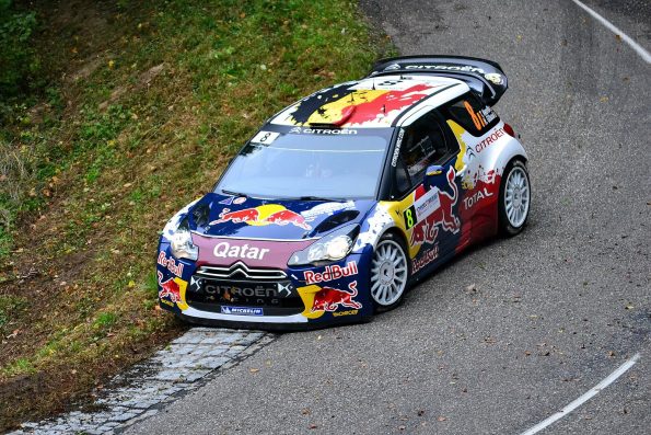 Thierry Neuville's Red Bull-liveried Citroën DS3 WRC, car 8, cornering on tarmac at the Rallye de France-Alsace in 2012, a Belgian flag painted on the roof and Qatar lettering on the nose.